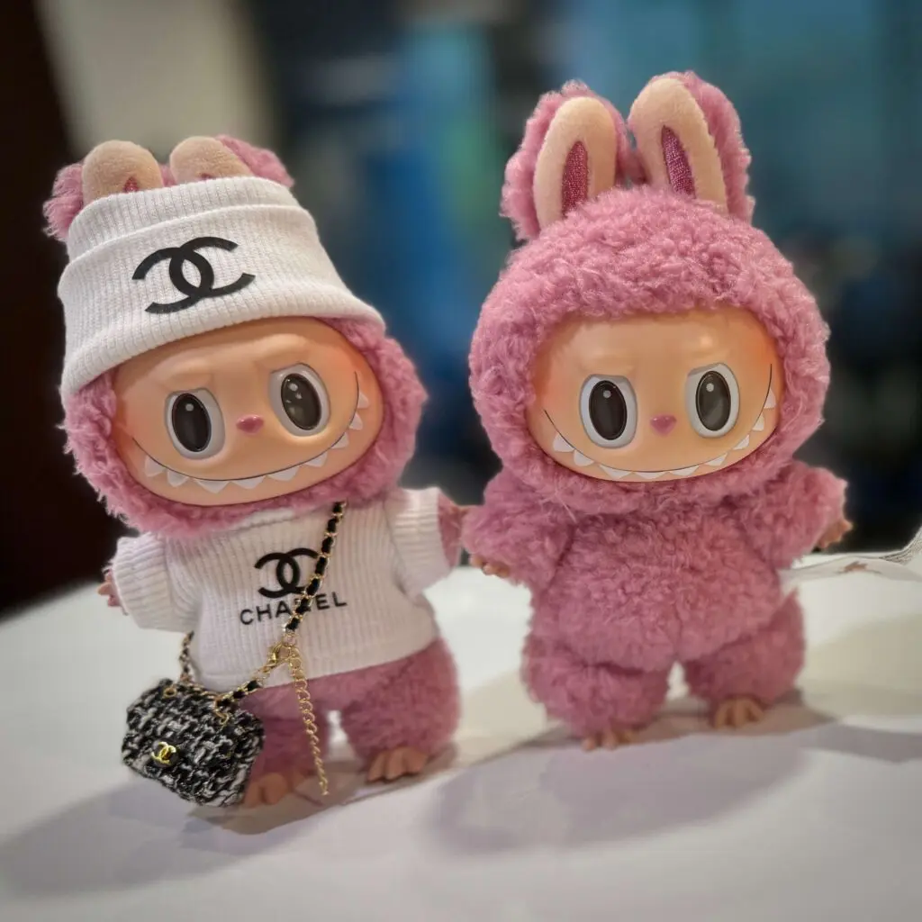 Two Labubu Lychee Berry side by side, one wearing a Chanel outfit and bag and one without an outfit