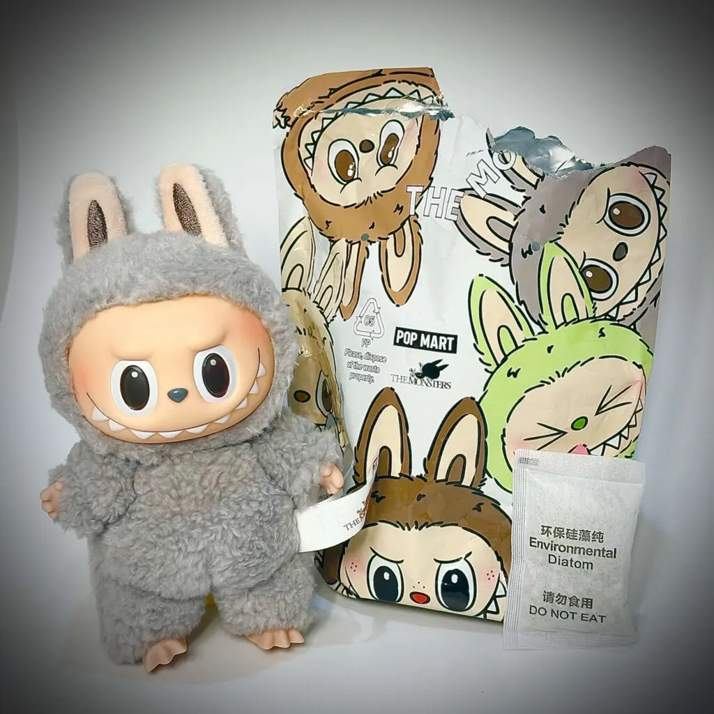 Labubu doll Sesame Bean from Exciting Macaron series standing next to pouch and dehumidification packet