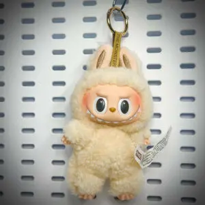 Labubu Soymilk doll from Exciting Macaron series hanging on a white pegboard