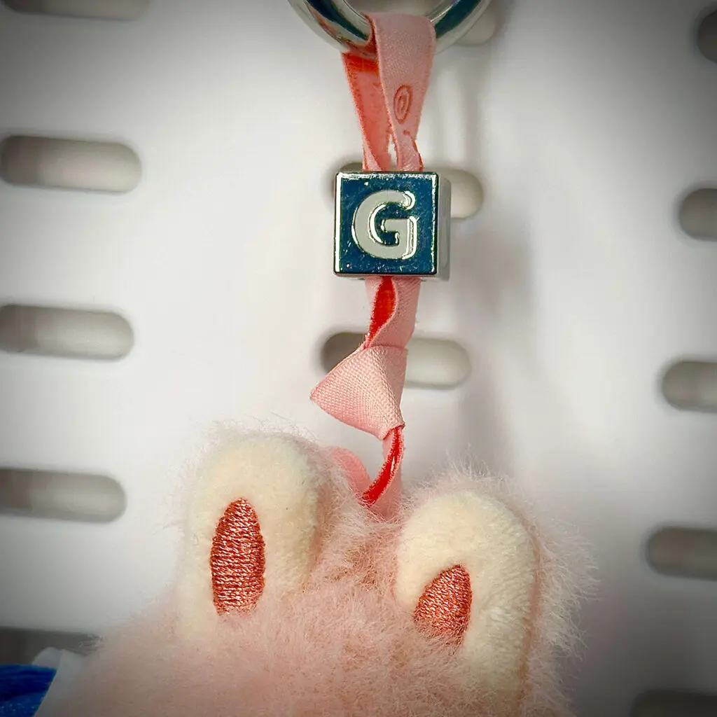 Labubu doll "G" close-up: The letter "G" engraved on the nugget that is attached to the lanyard (Pin for Love series)