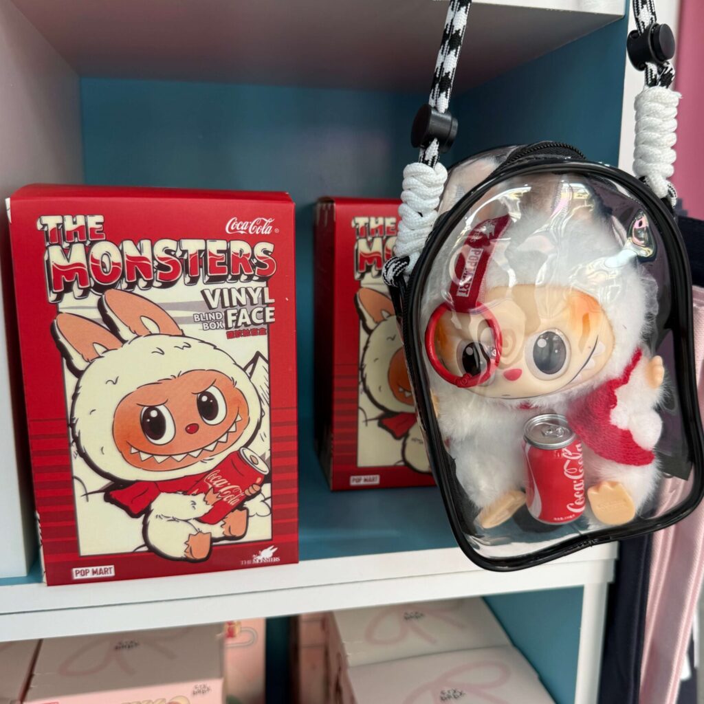 Fake Labubu Coca Cola doll inside a box next to another one in vinyl bag for sale at local gift shop