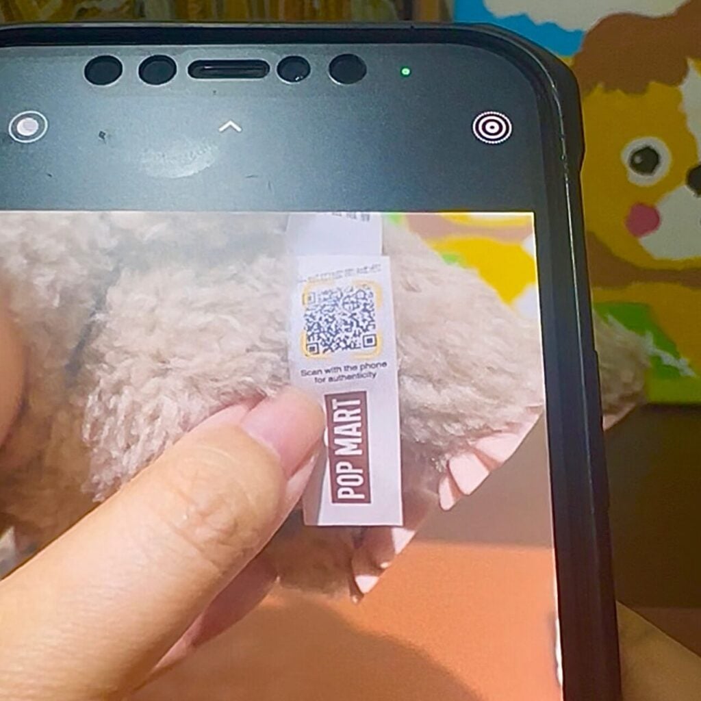 Instructions on where to find the QR code to scan on the tag of a Labubu doll